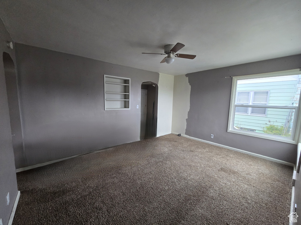 Carpeted spare room featuring arched walkways, ceiling fan, baseboards, and built in shelves