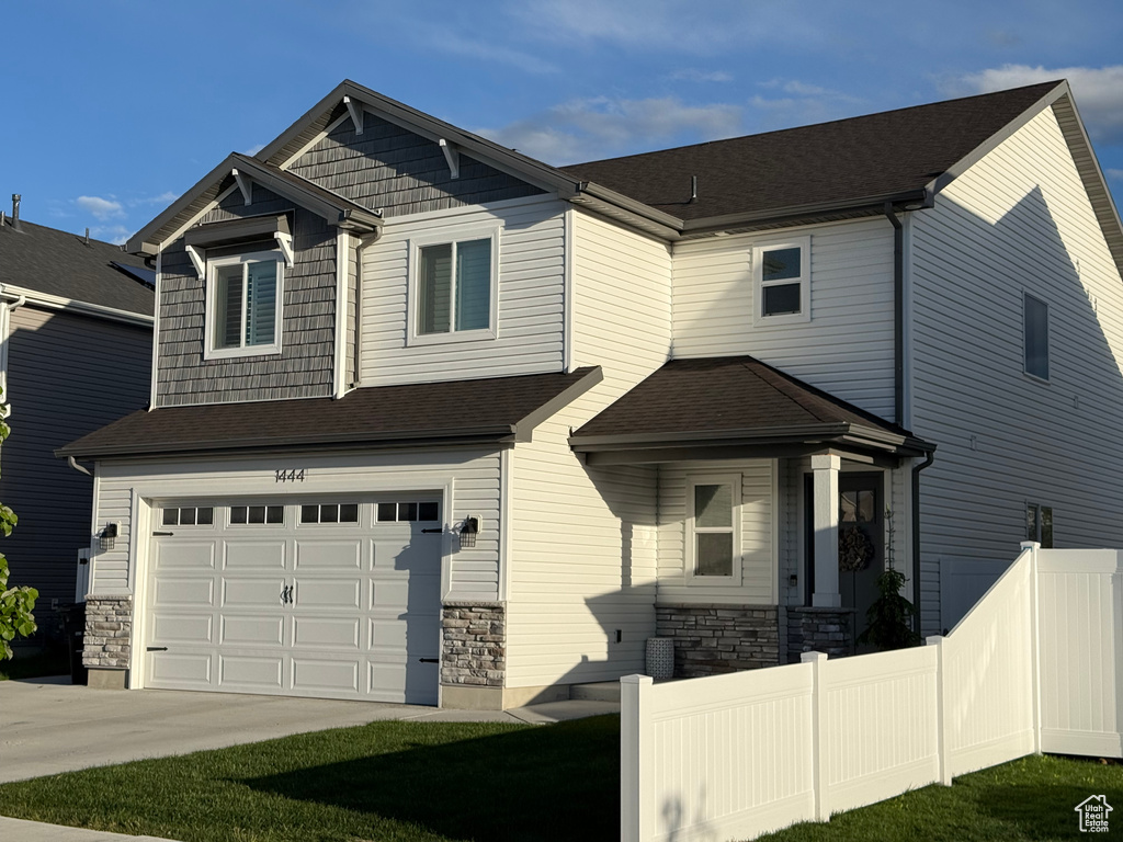 Craftsman inspired home with fence, a garage, stone siding, and concrete driveway