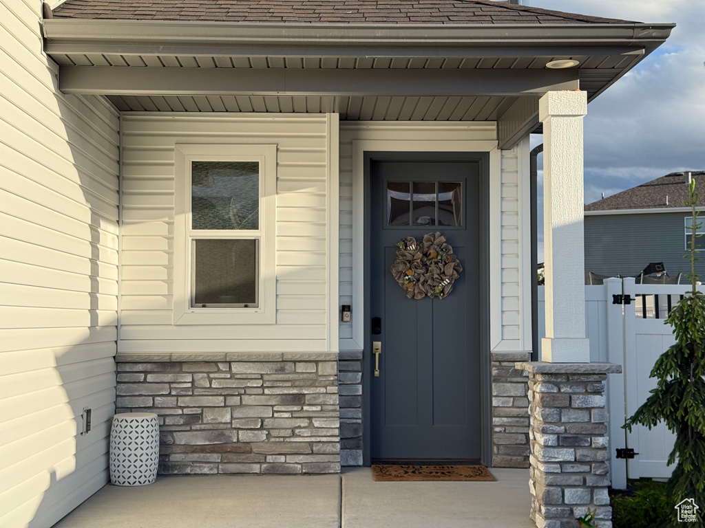 Doorway to property with stone siding, a shingled roof, and fence
