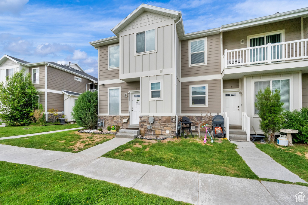 Multi unit property with board and batten siding, a front lawn, a balcony, and stone siding