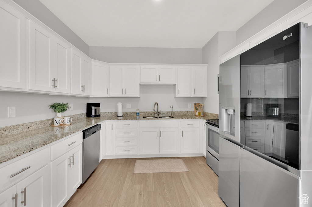Kitchen with a sink, appliances with stainless steel finishes, white cabinetry, light wood-type flooring, and light stone counters