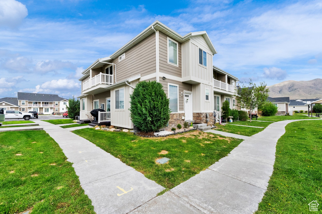 View of side of home with a balcony, a yard, a residential view, and stone siding