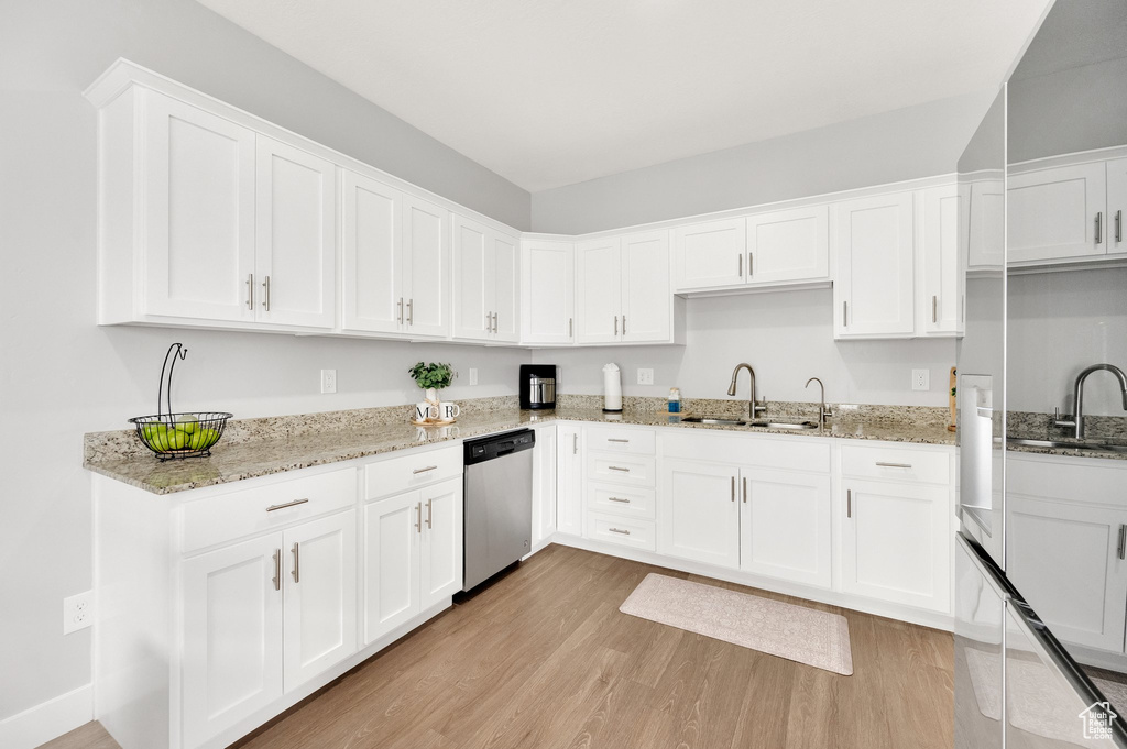 Kitchen featuring stainless steel dishwasher, a sink, light wood-type flooring, white cabinetry, and light stone countertops