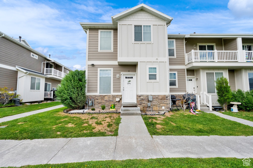 Townhome / multi-family property featuring board and batten siding, a front yard, and stone siding