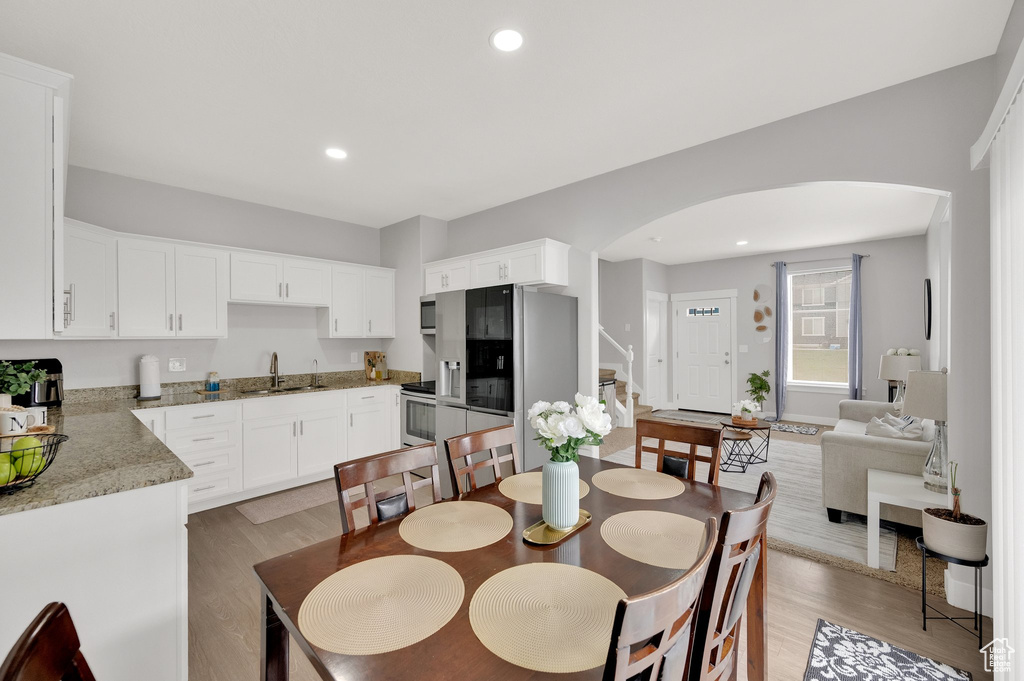 Dining room featuring arched walkways, light wood-style flooring, stairs, and recessed lighting