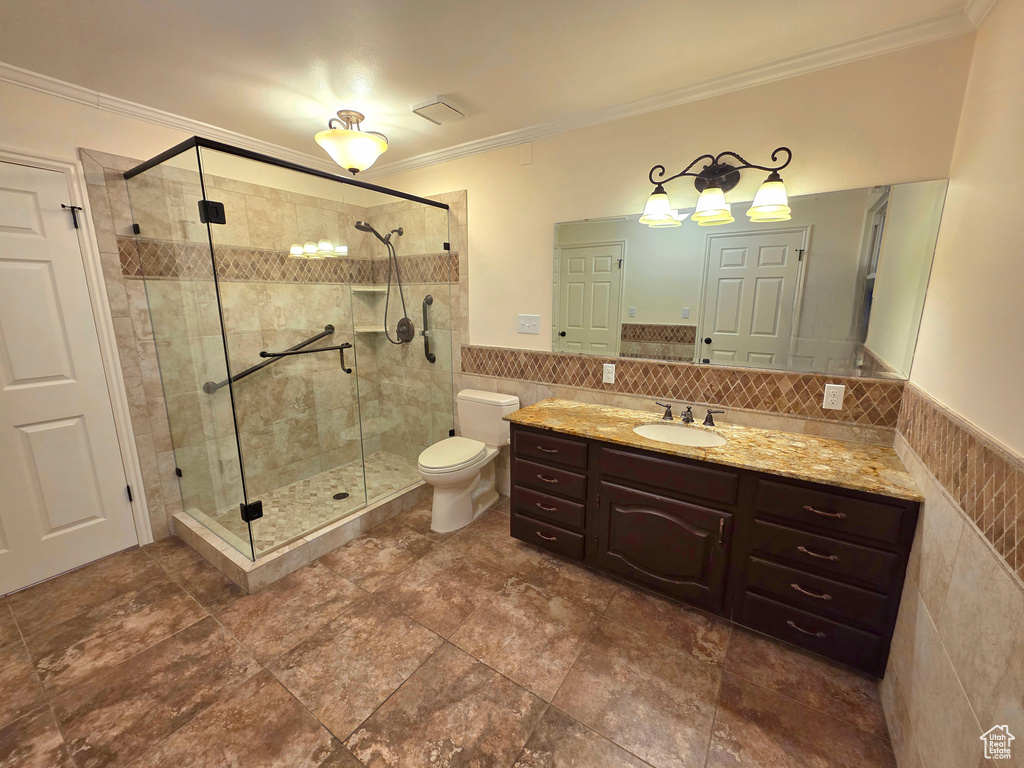Bathroom with a shower stall, crown molding, vanity, toilet, and tile walls