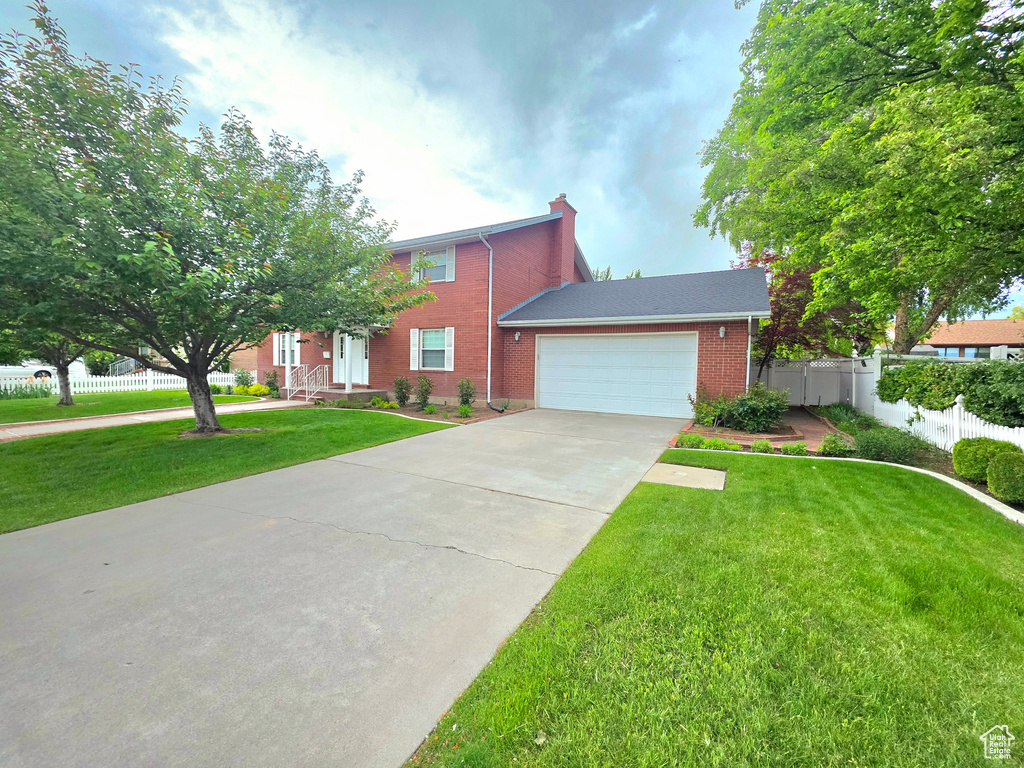 View of front of house with driveway, brick siding, an attached garage, and a chimney