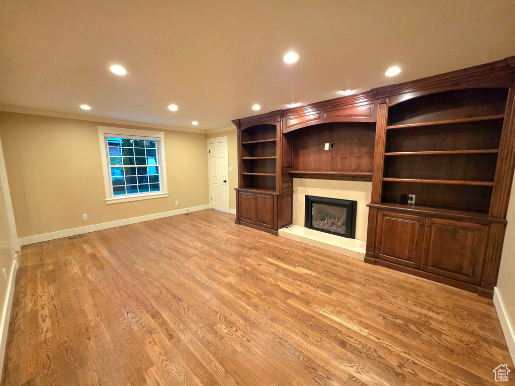 Unfurnished living room with recessed lighting, baseboards, ornamental molding, a fireplace with raised hearth, and light wood finished floors