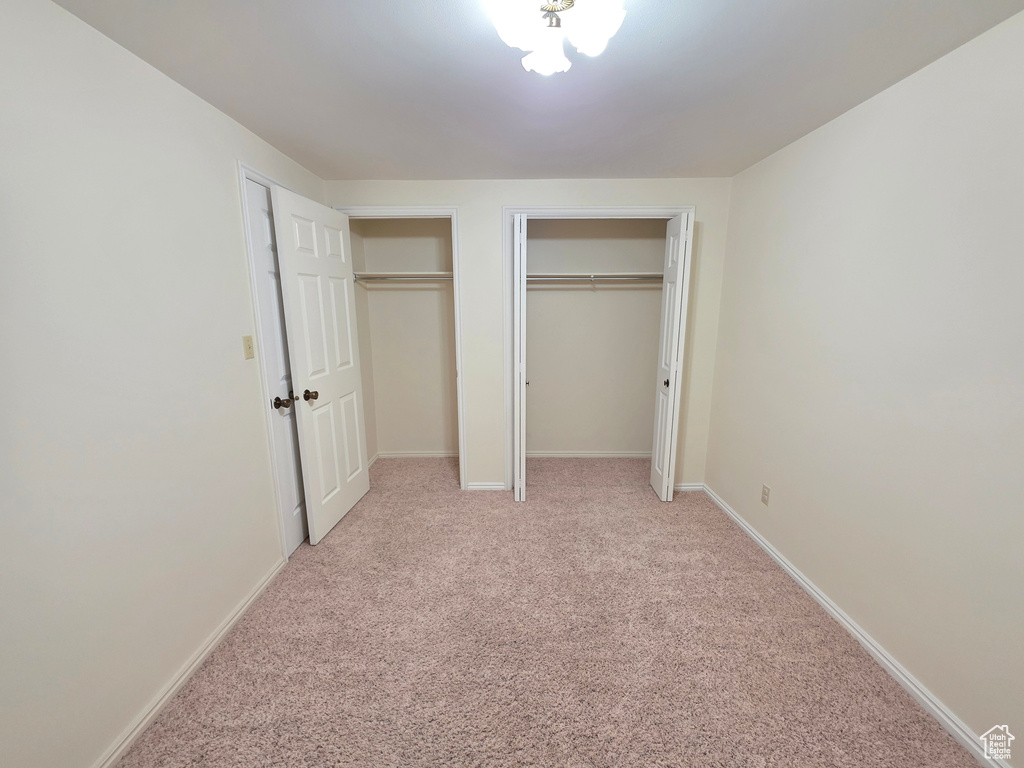 Unfurnished bedroom featuring multiple closets, light carpet, and baseboards