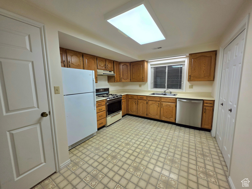 Kitchen featuring white appliances, a sink, brown cabinets, light countertops, and under cabinet range hood