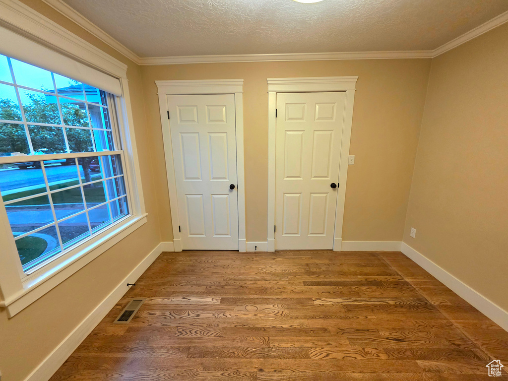 Unfurnished room with wood finished floors, crown molding, a textured ceiling, and baseboards