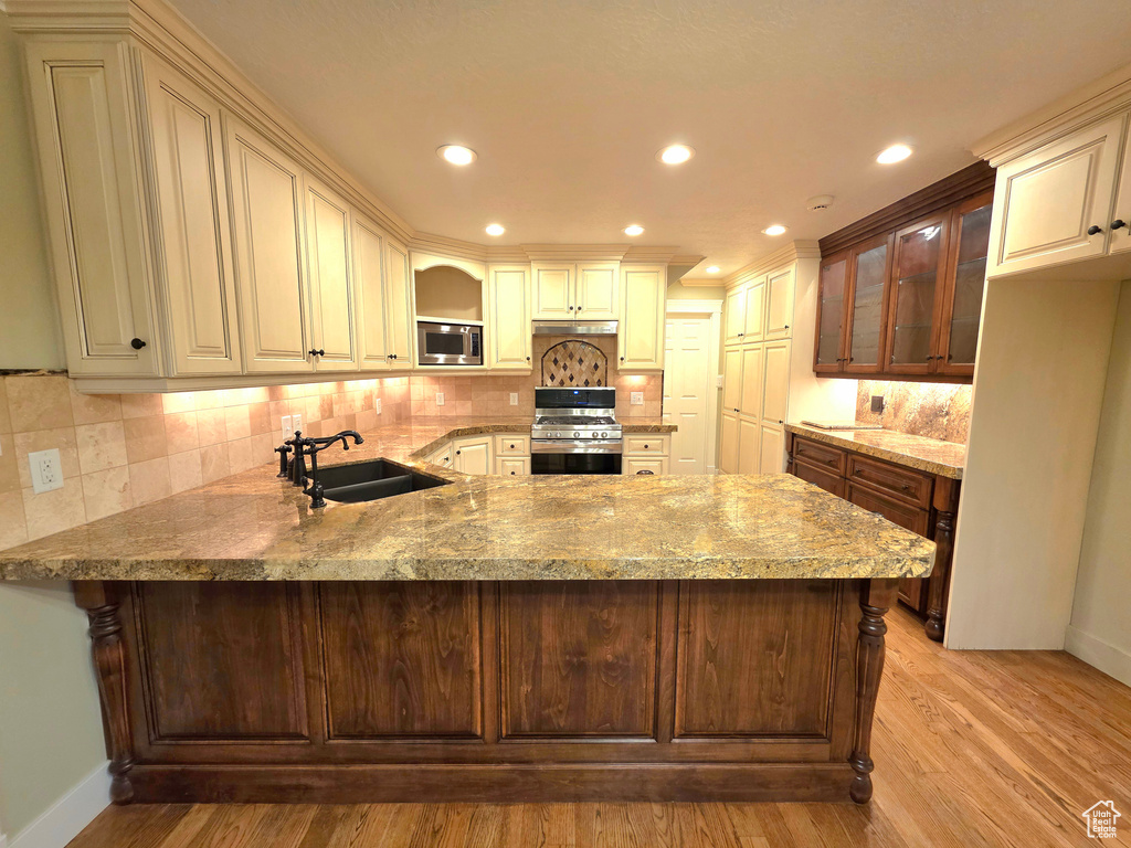 Kitchen with appliances with stainless steel finishes, a sink, a peninsula, baseboards, and recessed lighting
