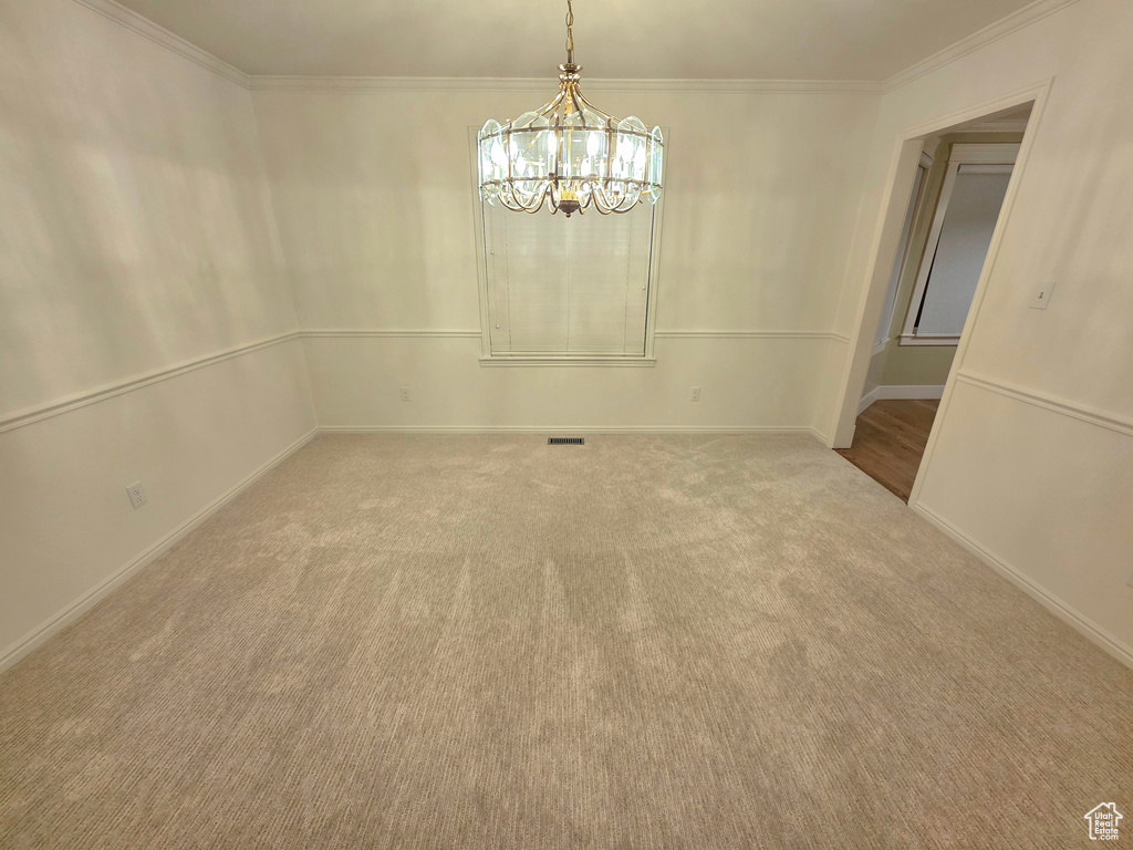 Carpeted spare room featuring a chandelier, crown molding, and baseboards