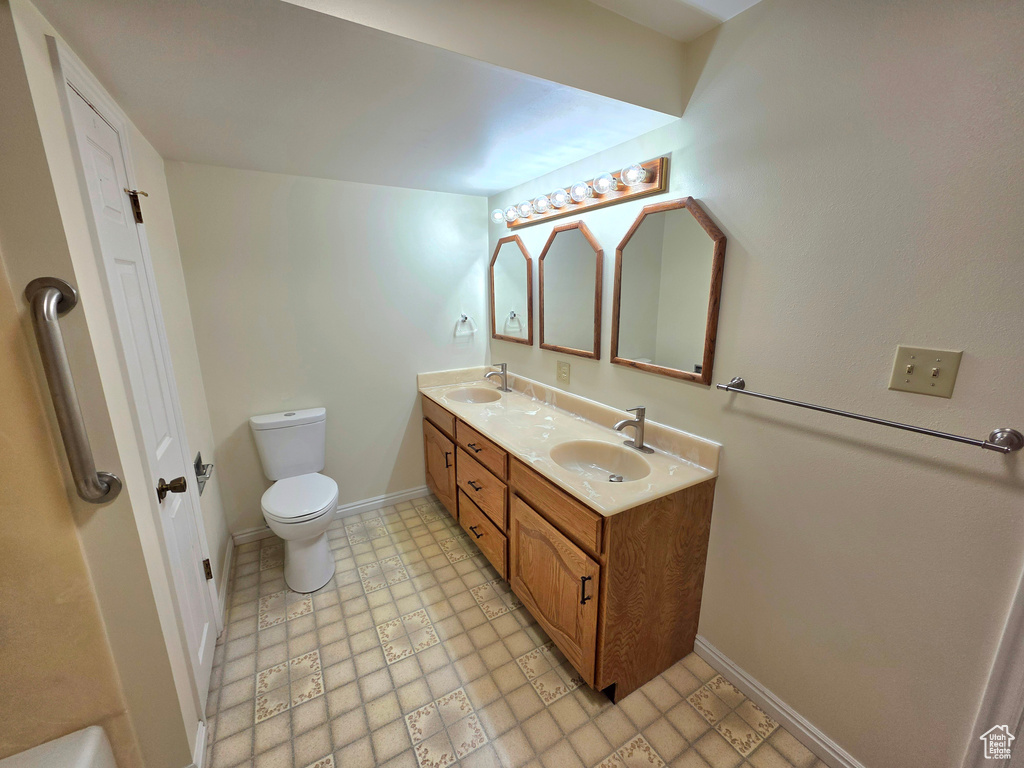 Full bathroom with toilet, double vanity, baseboards, and tile patterned floors