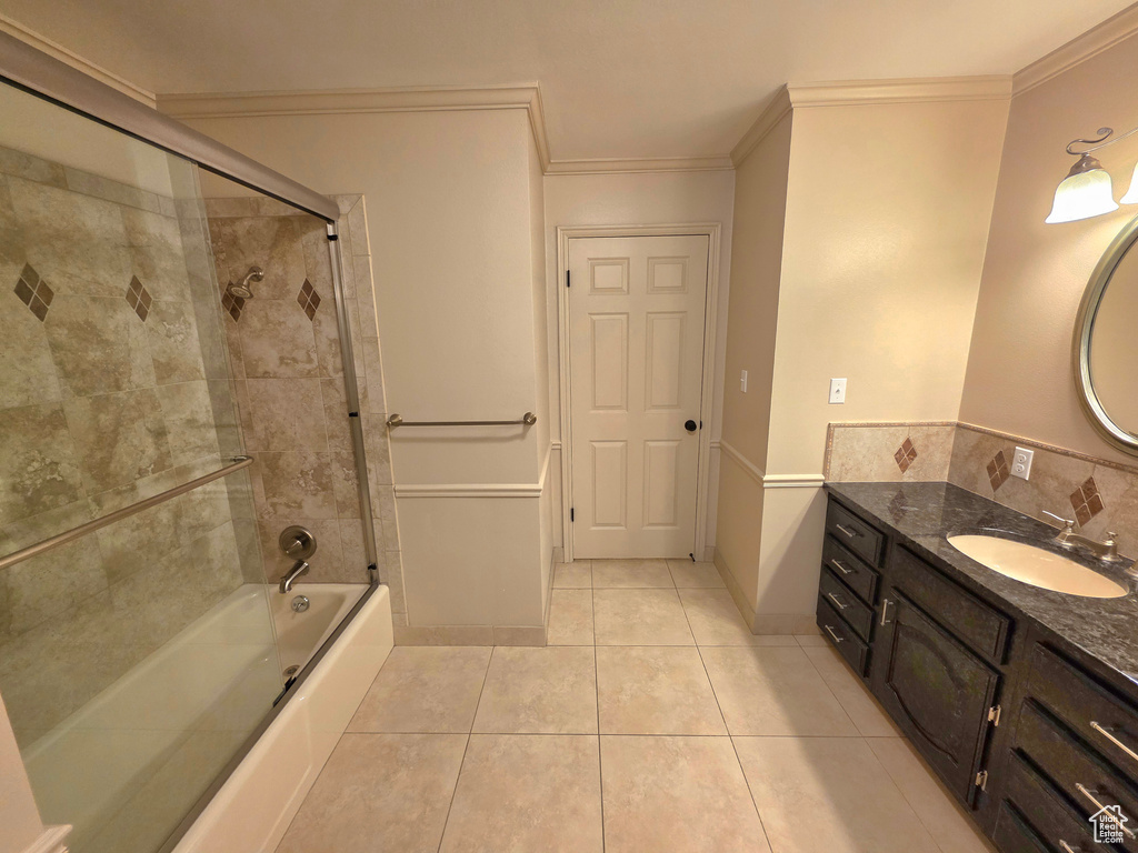 Full bathroom featuring tile patterned floors, combined bath / shower with glass door, ornamental molding, vanity, and baseboards