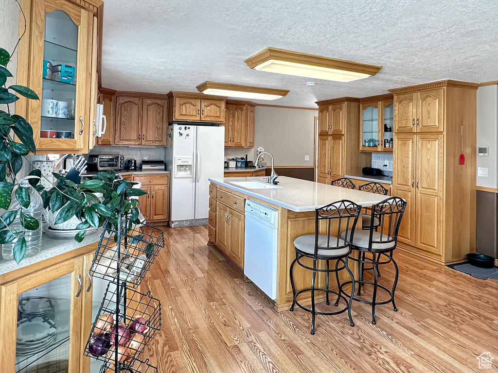 Kitchen featuring white appliances, a sink, light wood-style flooring, light countertops, and glass insert cabinets