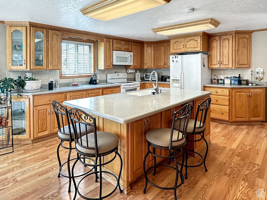 Kitchen with white appliances, a textured ceiling, light wood-type flooring, light countertops, and a kitchen bar