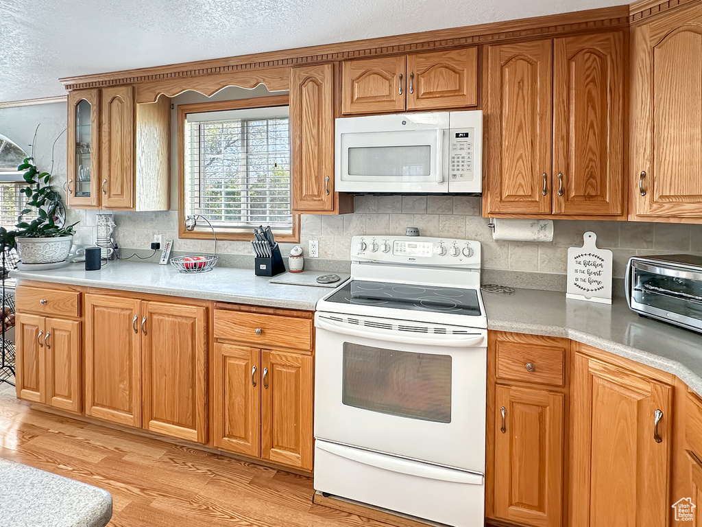 Kitchen with white appliances, backsplash, light wood-style flooring, light countertops, and a textured ceiling