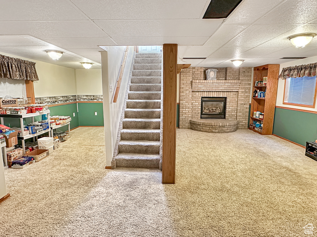 Basement with a drop ceiling, a fireplace, carpet flooring, stairs, and baseboards