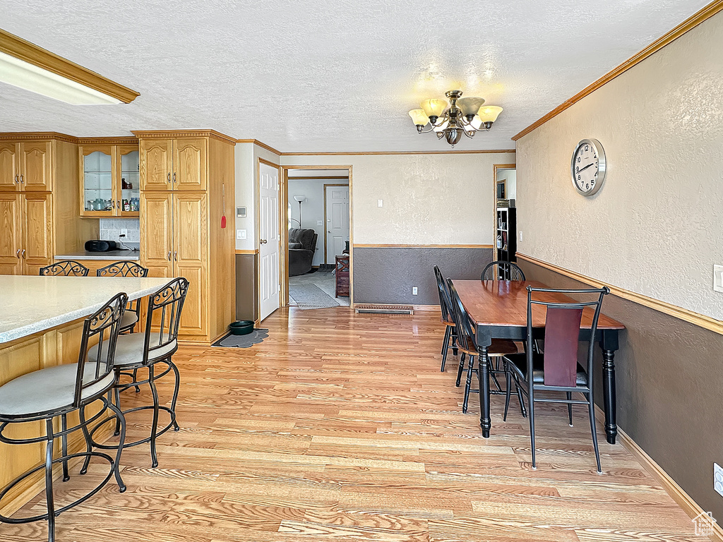 Dining area featuring a chandelier, light wood-style floors, a textured wall, a textured ceiling, and ornamental molding