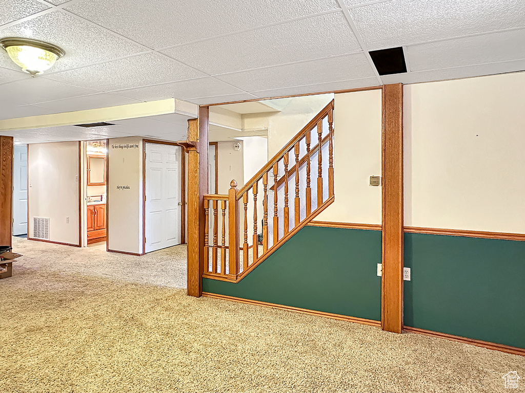 Finished basement with carpet flooring, stairway, and a paneled ceiling