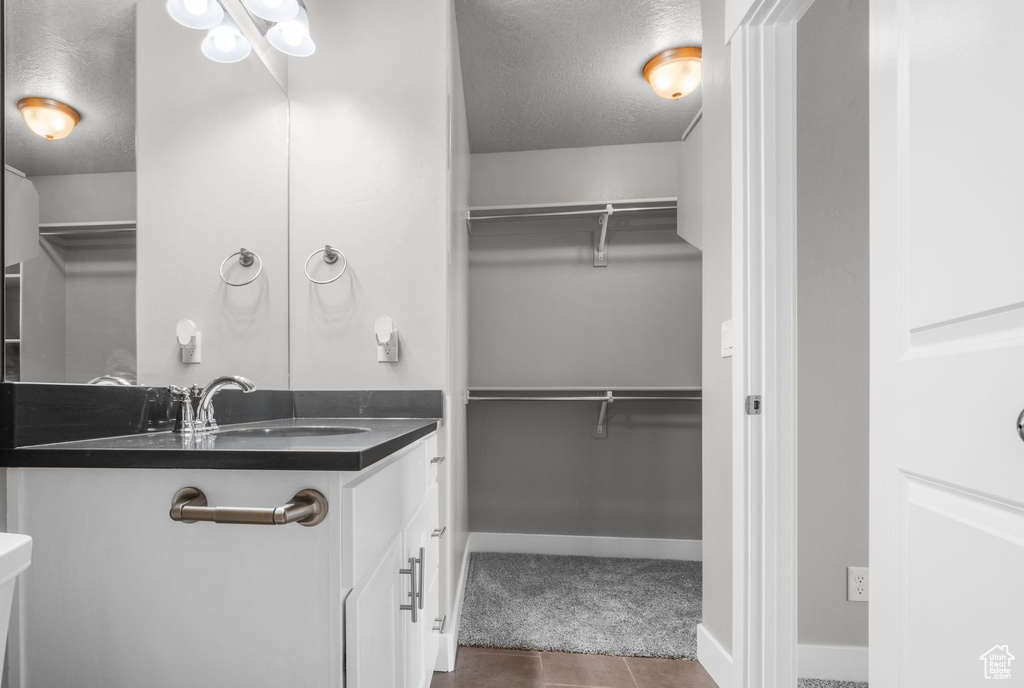Bathroom with a textured ceiling, vanity, baseboards, a spacious closet, and tile patterned flooring