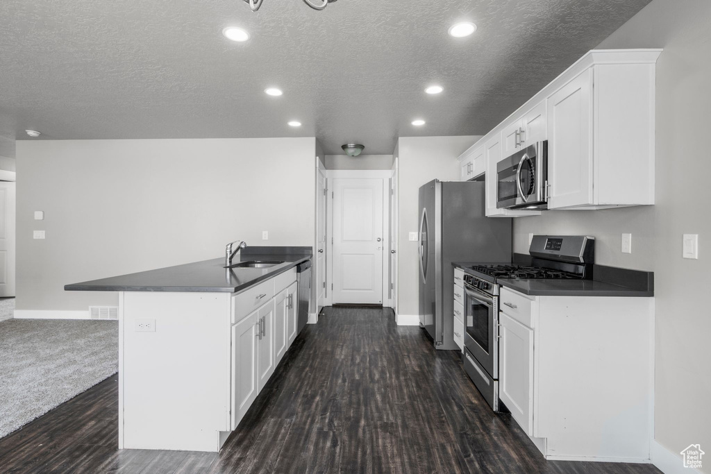 Kitchen featuring stainless steel appliances, a sink, dark countertops, a textured ceiling, and white cabinetry