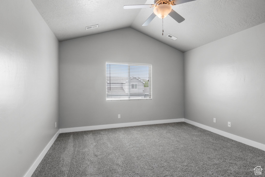 Carpeted spare room featuring ceiling fan, a textured ceiling, baseboards, and lofted ceiling