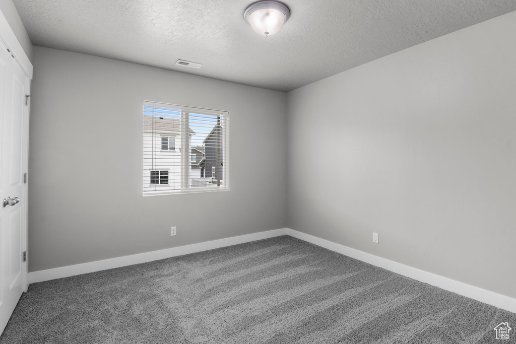 Carpeted empty room featuring a textured ceiling and baseboards