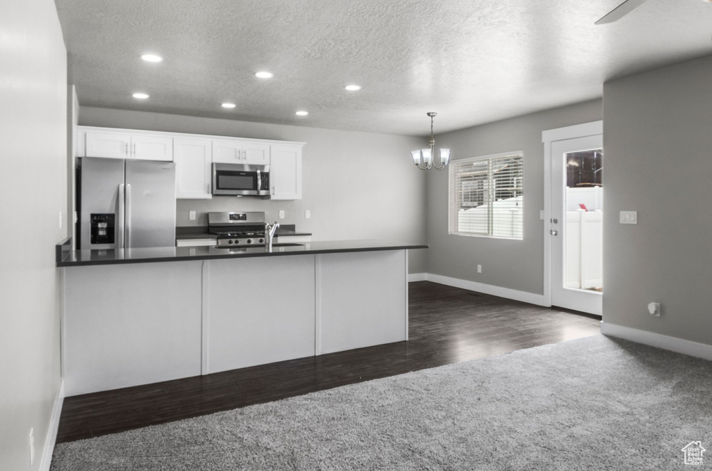 Kitchen featuring stainless steel appliances, dark colored carpet, baseboards, dark countertops, and a textured ceiling