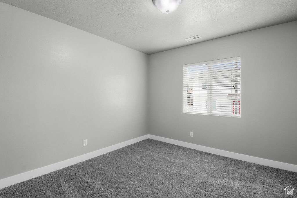 Spare room with a textured ceiling, dark colored carpet, and baseboards