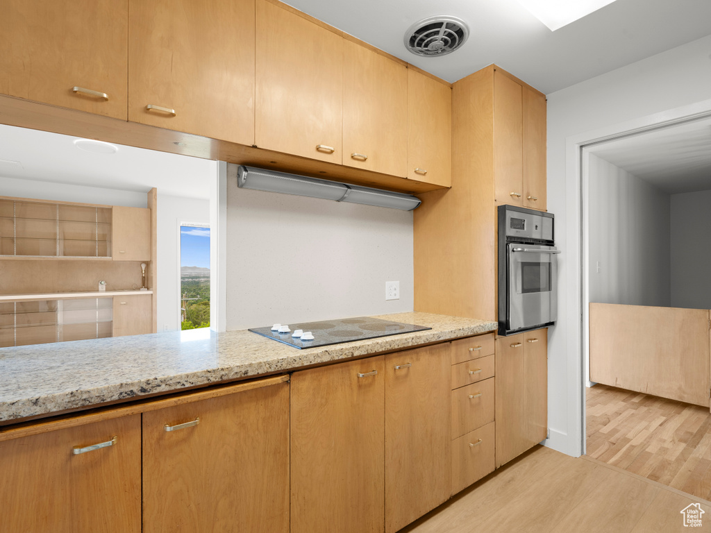 Kitchen featuring stainless steel oven, black electric cooktop, light wood-style floors, light stone counters, and light brown cabinets