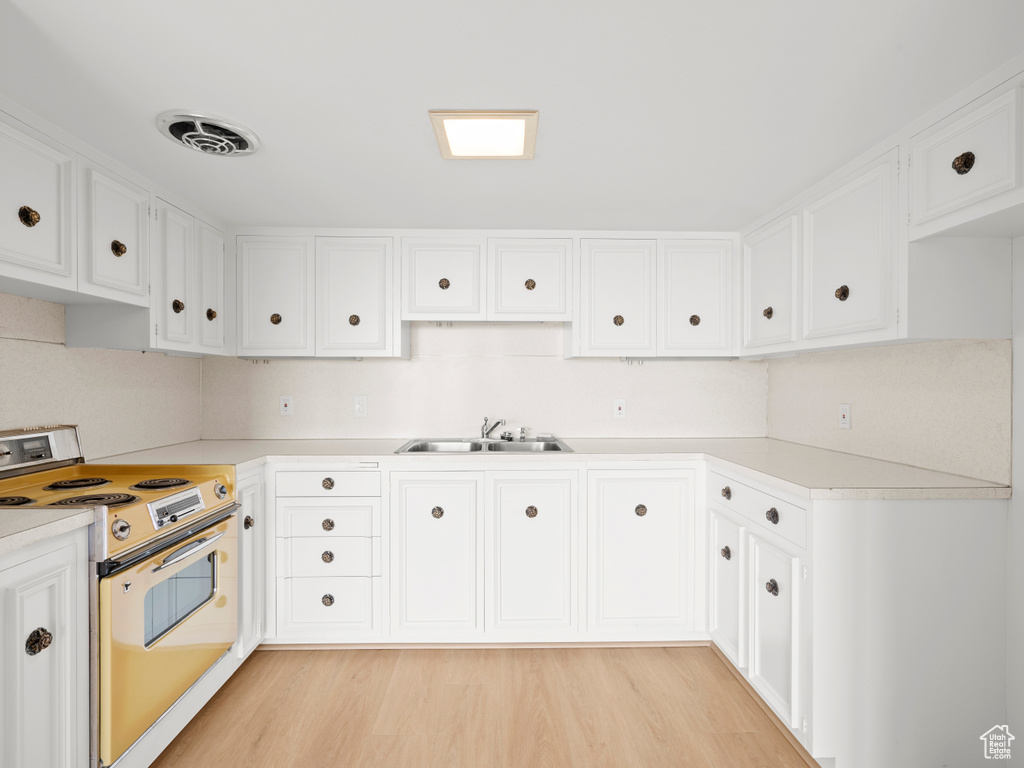 Kitchen featuring white electric stove, a sink, light countertops, and light wood-style floors
