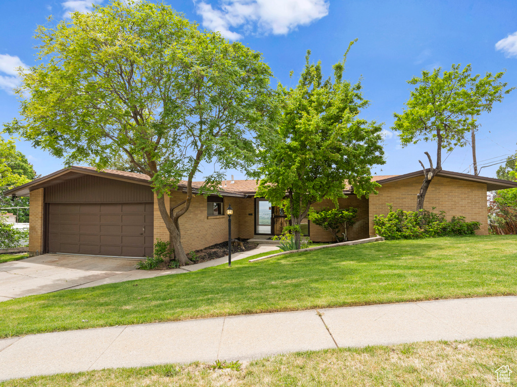 View of front of home with an attached garage, concrete driveway, brick siding, and a front lawn
