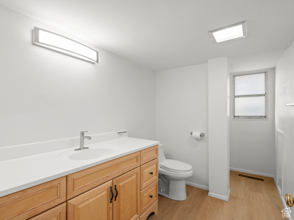 Bathroom with wood finished floors, toilet, vanity, and baseboards