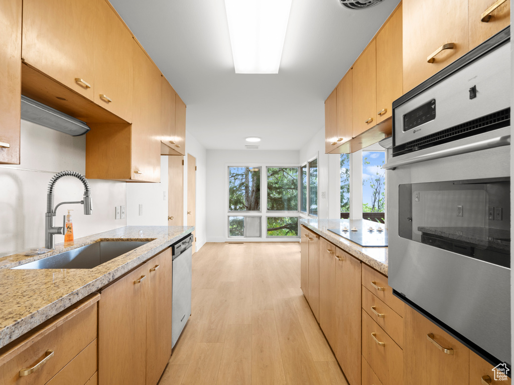 Kitchen with stainless steel appliances, a sink, light wood-style floors, light stone countertops, and light brown cabinetry