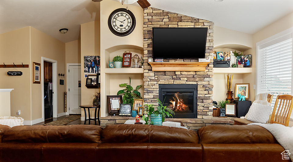 Living room with a stone fireplace, lofted ceiling, ceiling fan, and built in shelves
