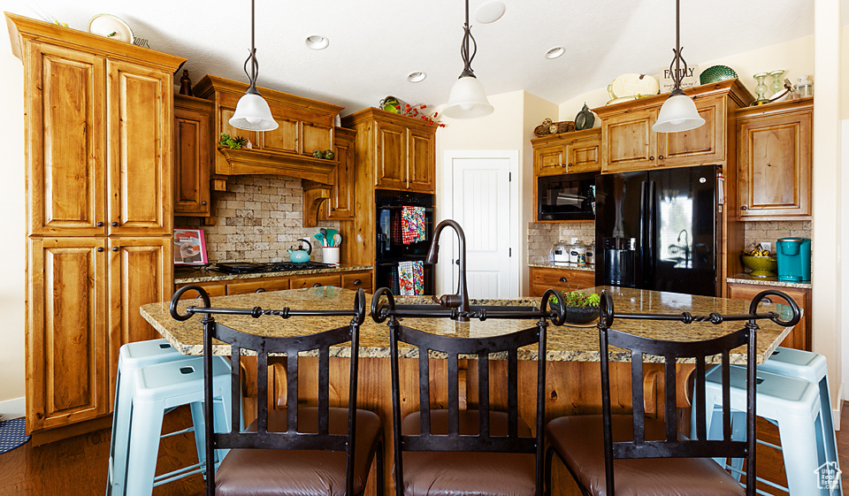 Kitchen featuring black appliances, an island with sink, backsplash, a breakfast bar, and recessed lighting