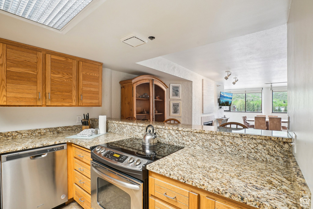 Kitchen featuring appliances with stainless steel finishes, light stone countertops, and a peninsula