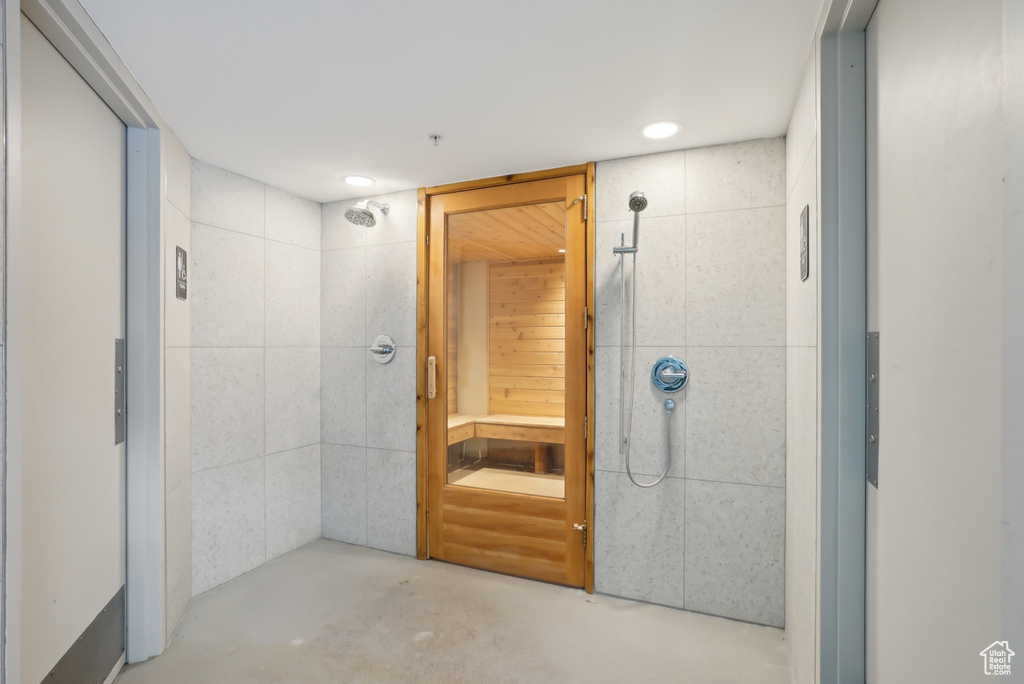 Full bathroom with finished concrete floors, tiled shower, elevator, recessed lighting, and tile walls