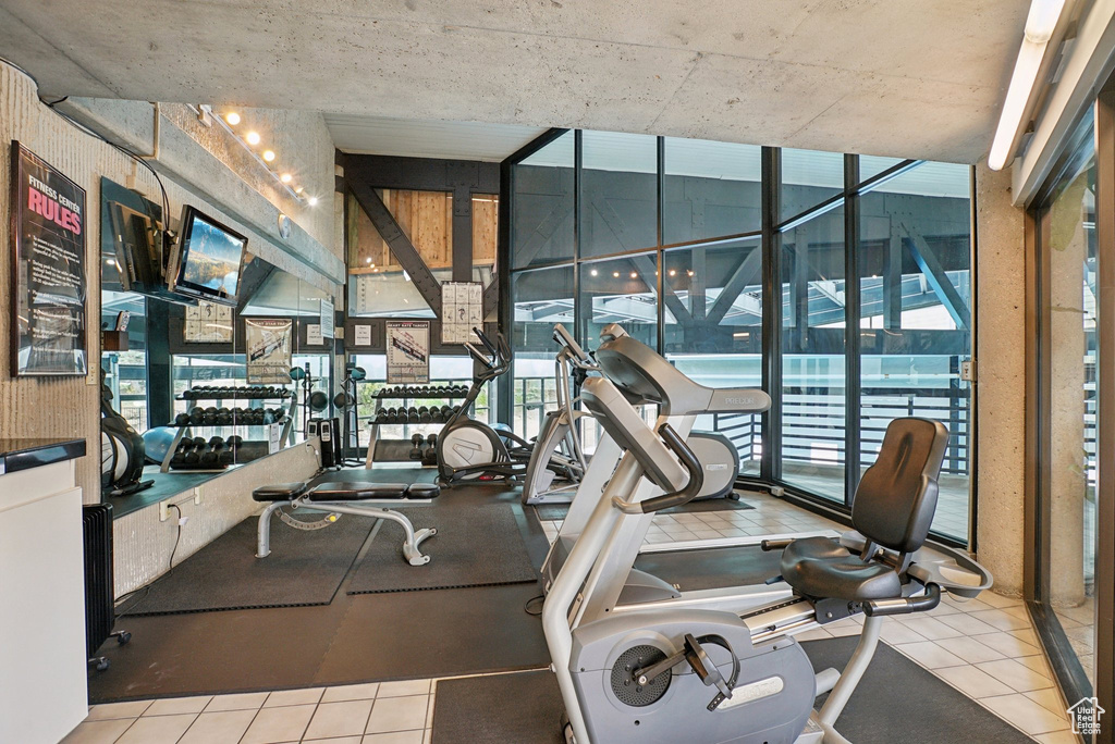 Gym with floor to ceiling windows, healthy amount of natural light, and tile patterned flooring
