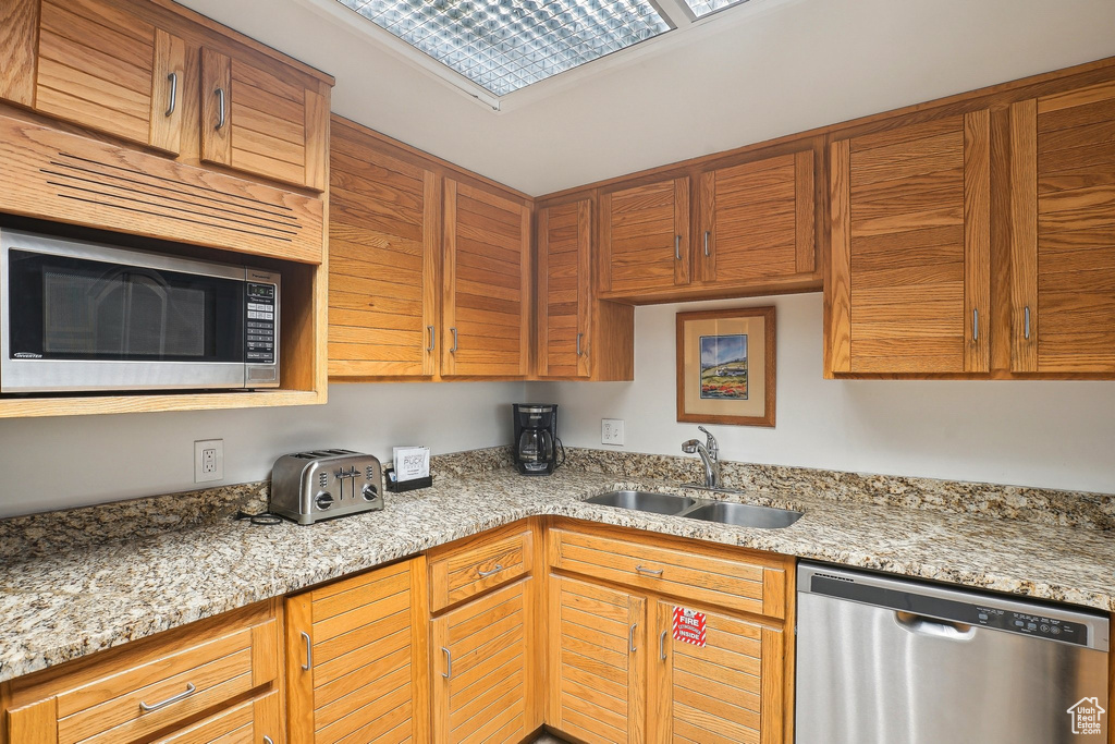 Kitchen with appliances with stainless steel finishes, a sink, and light stone counters