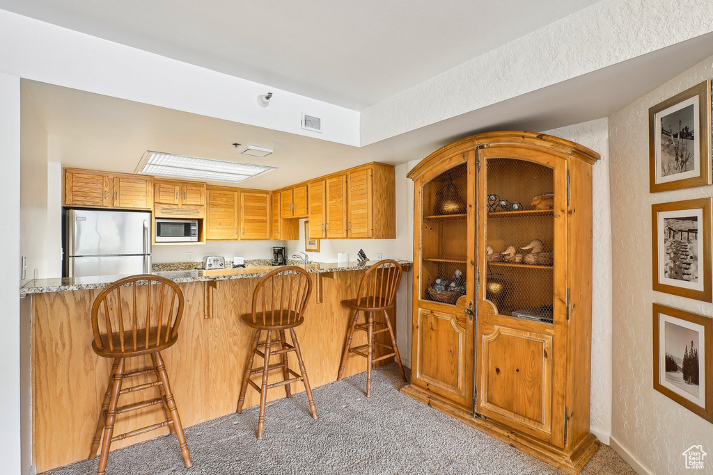 Kitchen with stainless steel appliances, light stone countertops, carpet flooring, a peninsula, and a textured wall