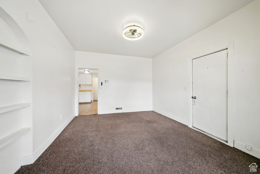 Carpeted spare room featuring built in shelves and baseboards