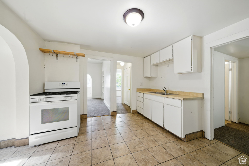 Kitchen featuring white range with gas cooktop, a sink, arched walkways, light countertops, and light tile patterned flooring