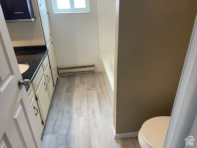 Bathroom featuring baseboard heating, wood finished floors, toilet, vanity, and a tub