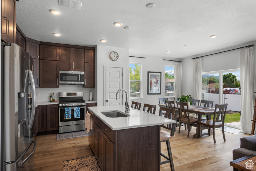 Kitchen with appliances with stainless steel finishes, a sink, light countertops, a breakfast bar area, and recessed lighting