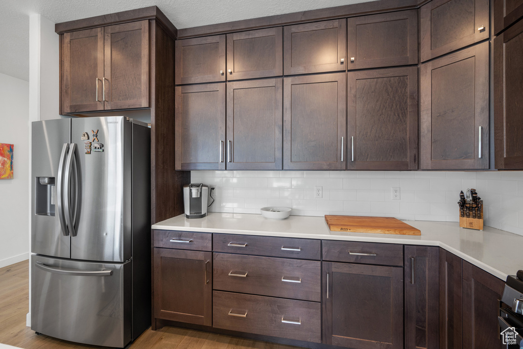 Kitchen with stainless steel fridge with ice dispenser, tasteful backsplash, and dark brown cabinets