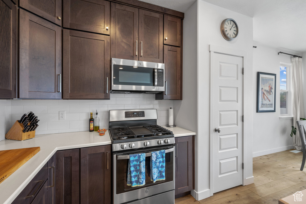 Kitchen featuring stainless steel appliances, dark brown cabinetry, backsplash, light wood-style floors, and light countertops