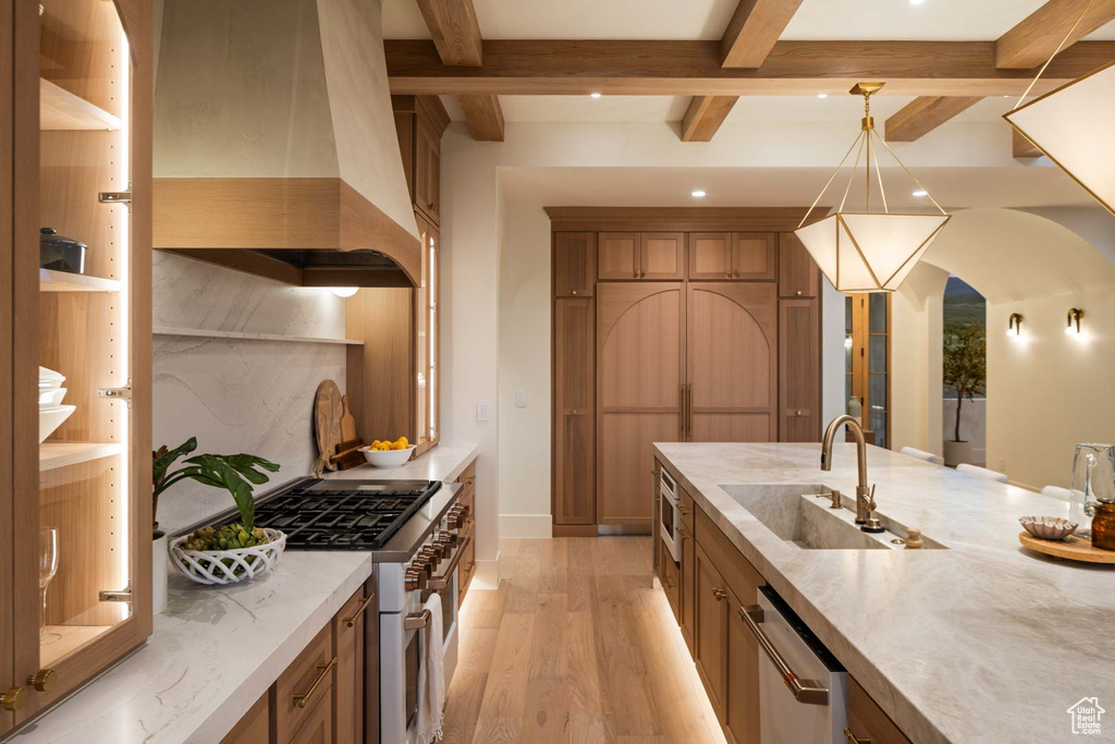 Kitchen with island range hood, appliances with stainless steel finishes, a sink, arched walkways, and light wood-style flooring